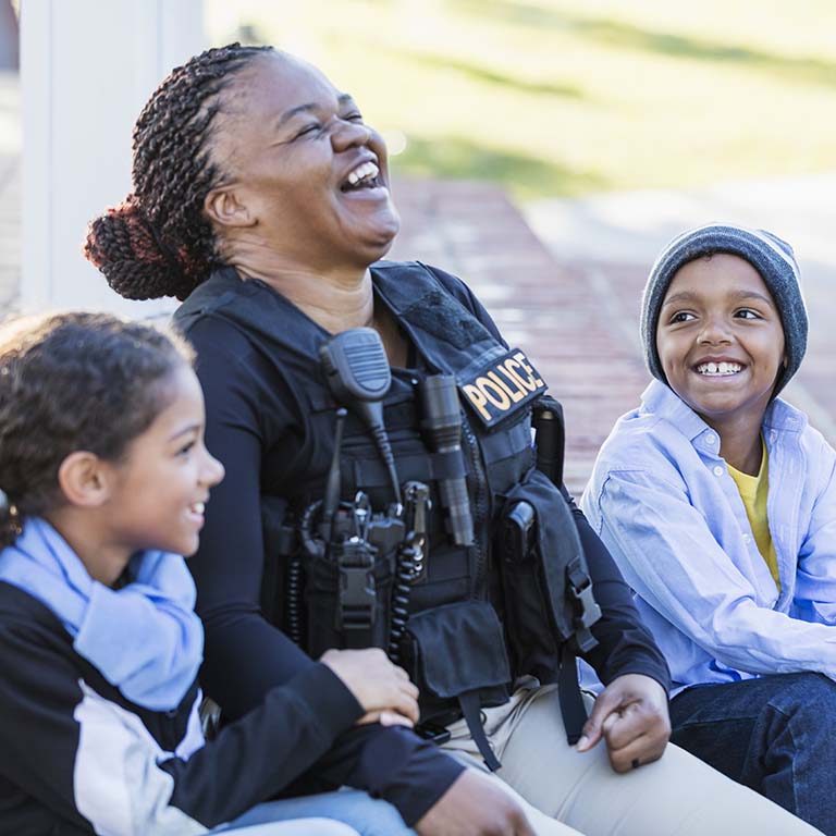 Laughing police officer with two children outside on a sunny day