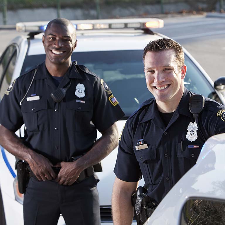 Two smiling police officers standing next to police vehicles