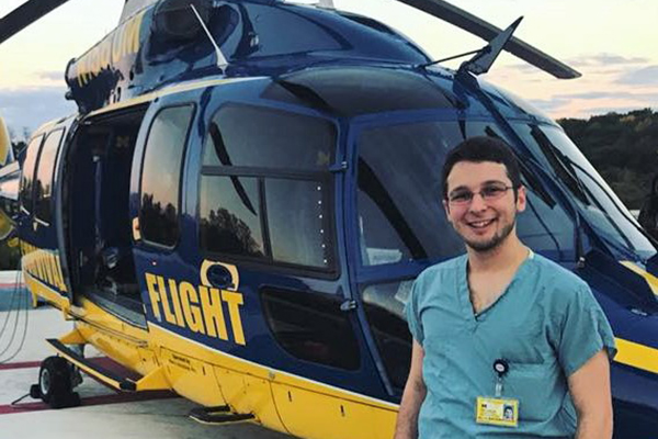 Ali Bacharouch standing in hospital scrubs in front of a helicopter