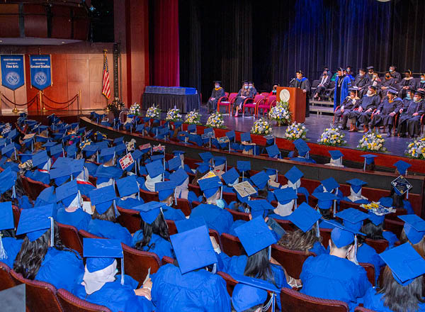 Image of graduates seated in auditorium, dignitaries on stage