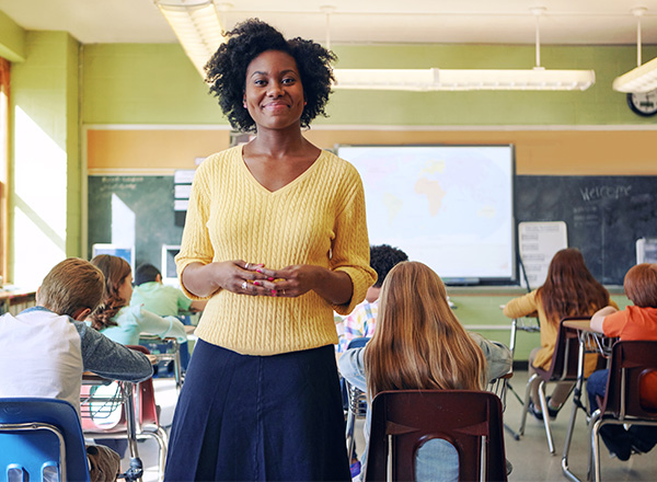 An African-American woman in a classroom surrounded by school-age children. 