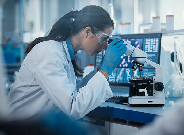 Woman wearing lab coat, looking into microscope