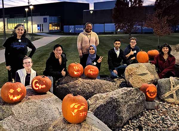 Photo of carved pumpkins on rocks, smiling people showing off their carvings.