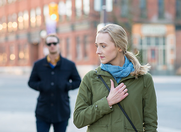 Young woman looking over her shoulder at a stranger who is following her in a city.