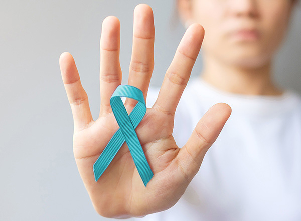 Woman in background, palm in foreground with teal ribbon. 