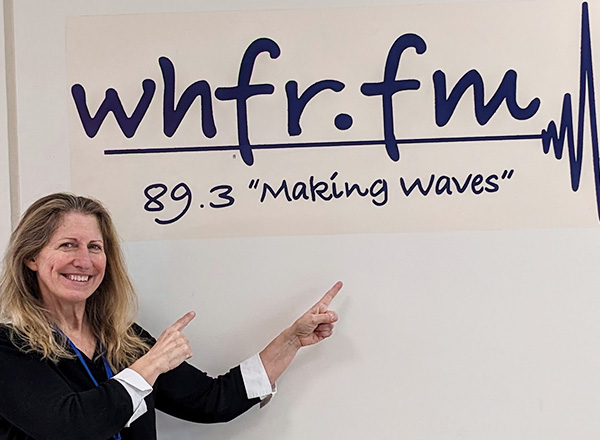 Susan McGraw proudly stands in front of the WHFR-FM sign in the Student & Culinary Arts Center. 