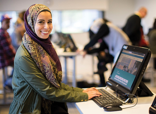 A smiling student using a computer in a Welcome Center lab.