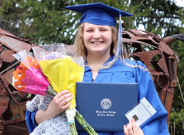 A picture of AnnMarie Dill smiling in her cap and gown, holding two bouquets of flowers and her diploma. 