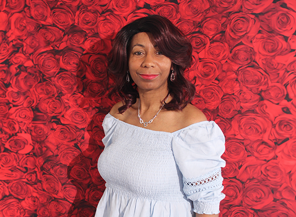 June Williams standing in front of a backdrop image of red roses.