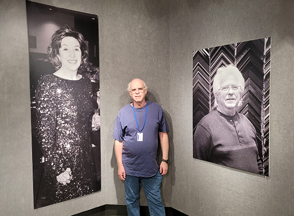 Steve Glaser stands in the middle of two large black and white portraits in the Sisson Gallery