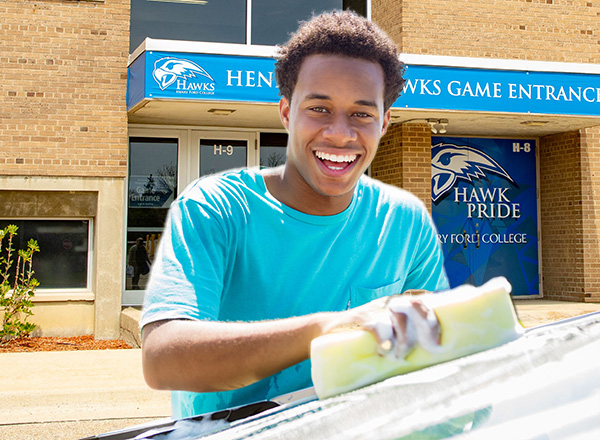 Smiling young man with a sponge washing a car in front of the Athletics Building on the HFC campus.