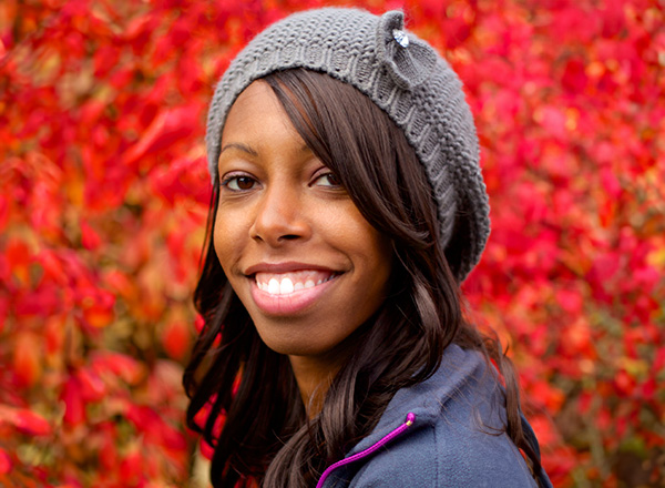 Jessica Shamberger wearing a grey beret and smiling in front of fall foliage. 