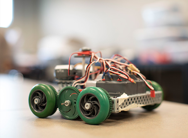 Image of a robot car that the Engineering Club created with wires, green rubber wheels, and metal.