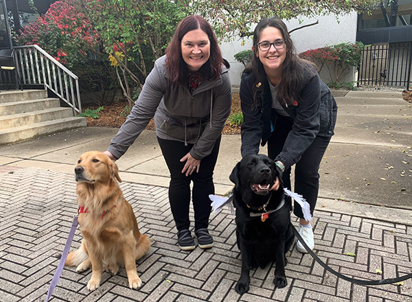 HFC employees Bridget and Laura smiling while enjoying therapy dogs Maui, a golden retriever, and Tango, a black lab.