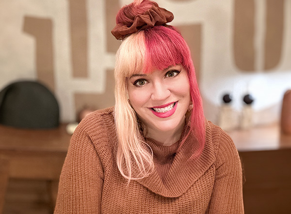 Courtney Spivak has spilt hair, blonde and pink, wearing a toffee colored sweater, smiling. 