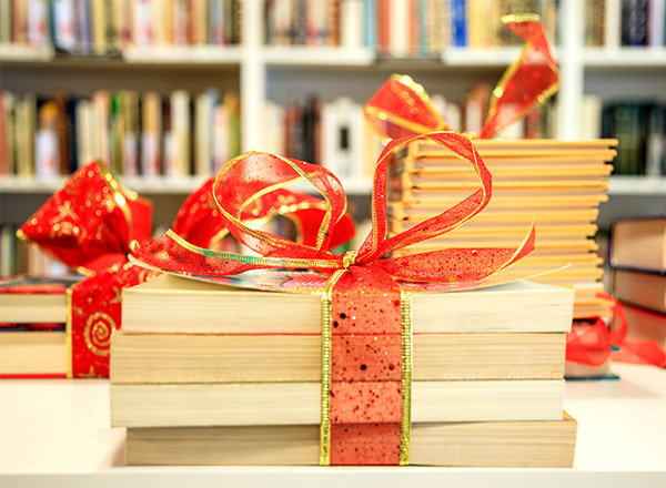 Stacks of books wrapped up in red and gold ribbon and bows with a shelf of books in the background.