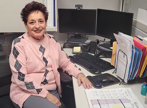 Marlene Wojtowicz, in a pink and grey argyle sweater, sits at her desk.