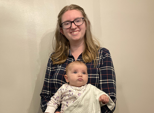 Sarah Kigar wearing glasses and a button-down shirt, holding a baby