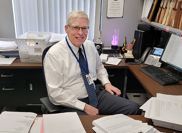 Fred Steiner sits at his desk which is piled high with paperwork.