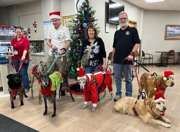 Jeremy Tabor and volunteers with their therapy dogs in holiday clothing and Santa hats.