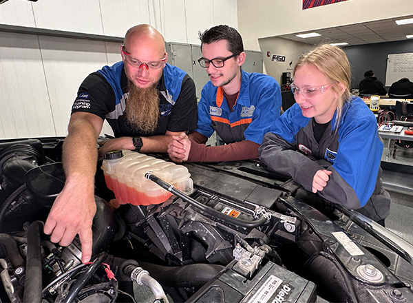 Instructor Kris Young and ASSET automotive program students looking under the hood of a vehicle.