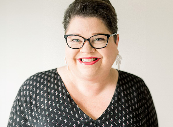 A headshot of Jaimie Hutchison, she has short dark hair, wearing black glasses and a black and white spotted shirt.