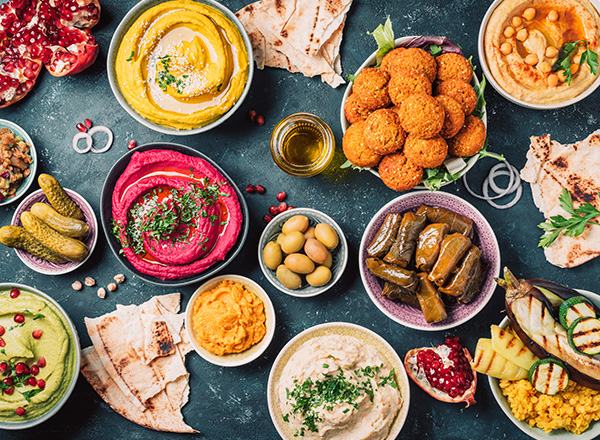 Middle Eastern food with pita, olives, colorful hummus, falafel, stuffed dolma, baba ganoush, pickles, vegetables, pomegranate, eggplants.
