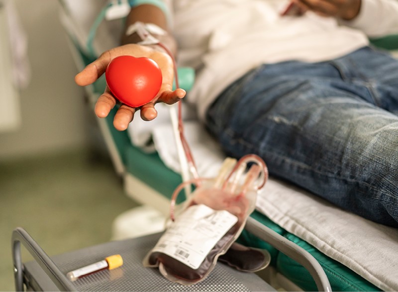 photo of a man giving blood and showing off a heart-shaped ornament. 