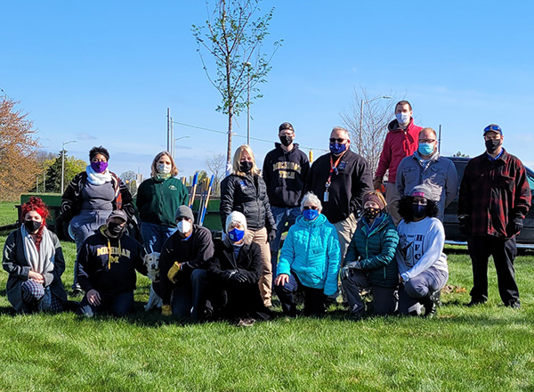A group of people outdoors wearing masks, preparing to plant trees