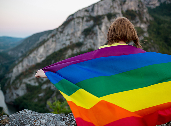 person looking at mountain scene, holding a pride flag