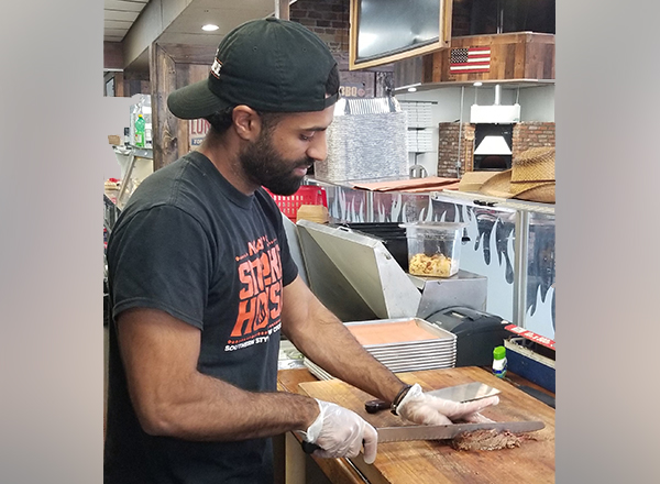 HFC alumnus and MRI technologist Noah Saleh, who co-owns Noah's Smokehouse in Dearborn, cuts some brisket. 