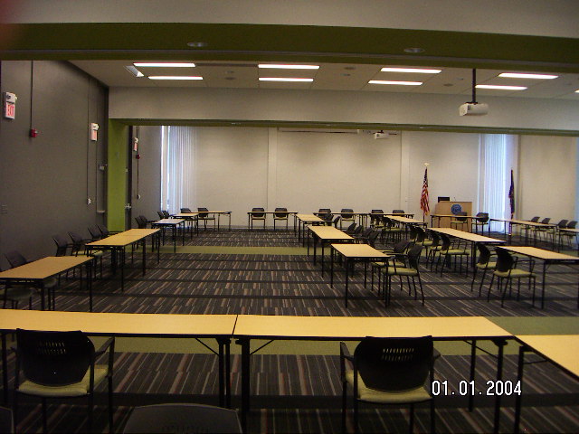 Inside of large room with rows of long, rectangular tables and a podium at the furthest end of the room