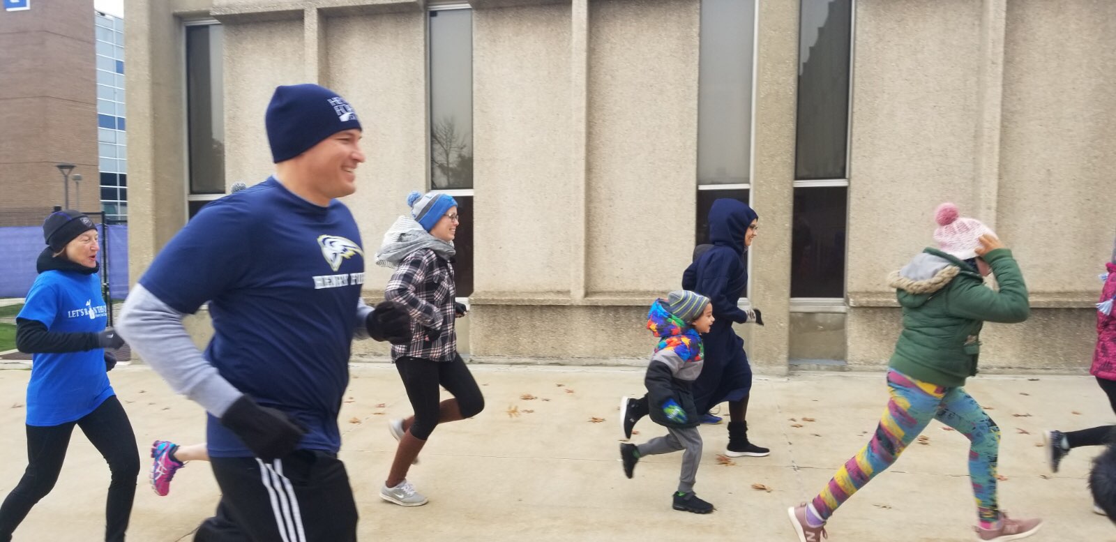 President Kavalhuna smiles as he runs through campus, accompanied by community members.