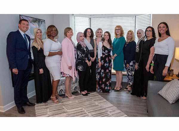 Karen Wilmering (fourth from left, dressed in pink) has been HFC's Interior Design program coordinator for 12 years. She's pictured here with President Russell Kavalhuna (left) and her students in the apartment home they redesigned at Henry Ford Village 
