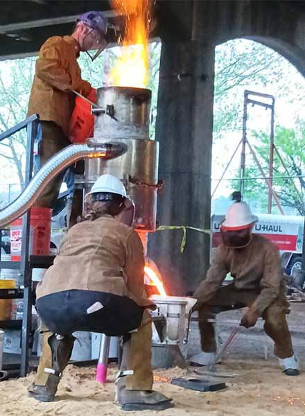 Members of the Ironic Femmes gather the hot metal after melting it. 