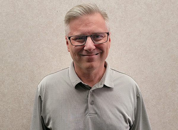 Shaun Stevens wearing a light grey polo shirt and glasses smiling.