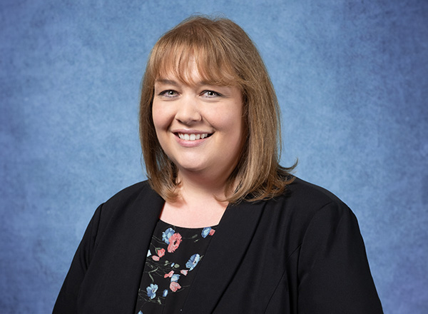 Julie Fountain in front of a blue background, wearing a black jacket with floral top.