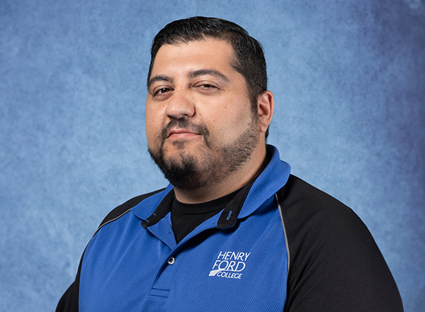 Samer Atris wearing a blue and black HFC shirt in front of a blue background.