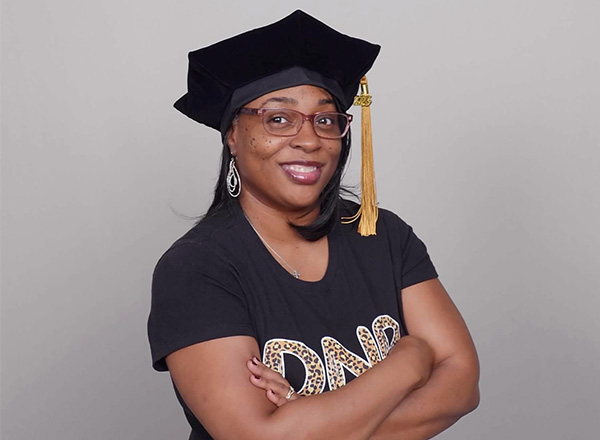 Candance Niemer wearing her graduation cap, standing with crossed arms.