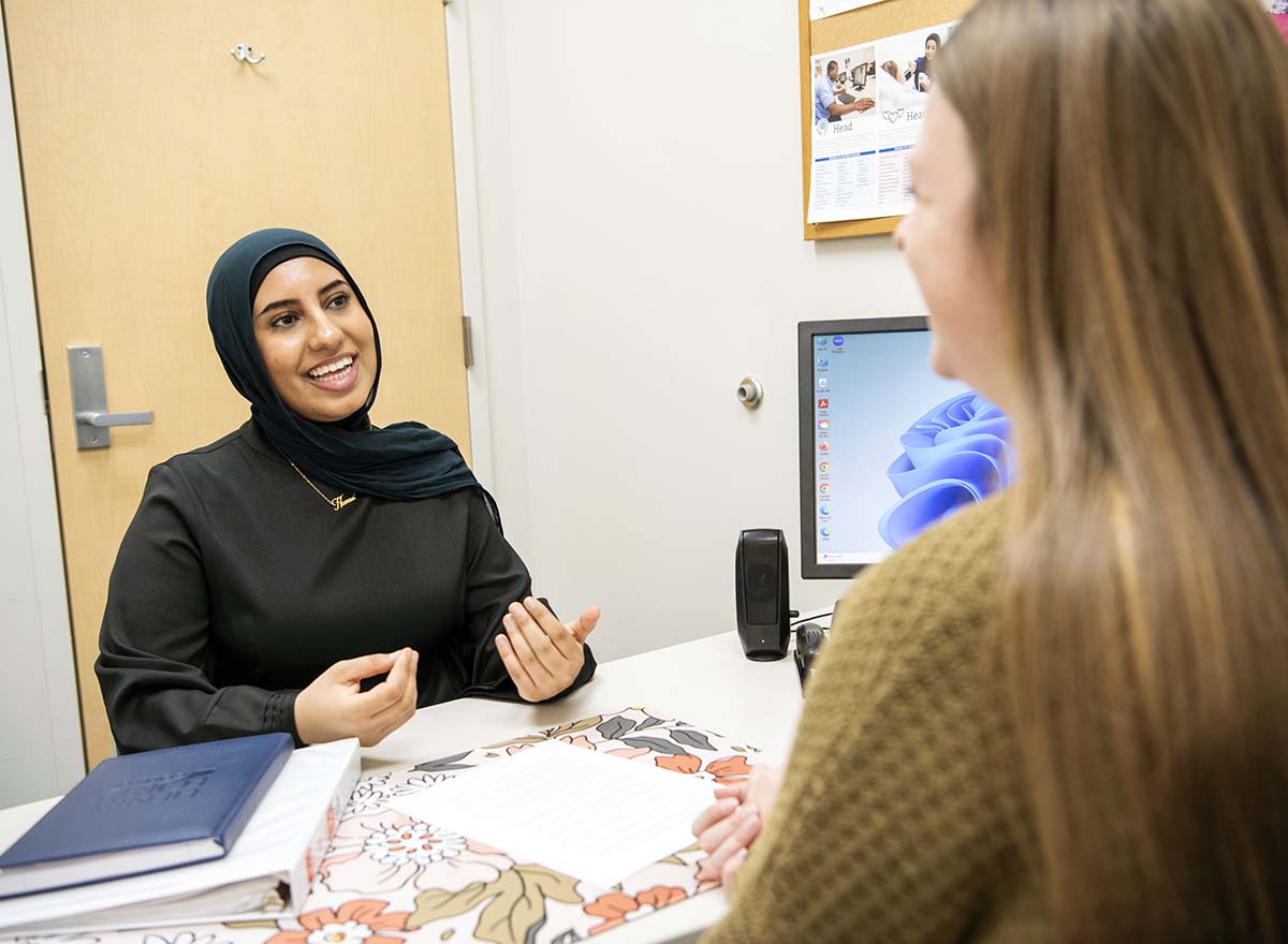 Student meeting with Advisor in office, sitting at a white desk smiling and talking