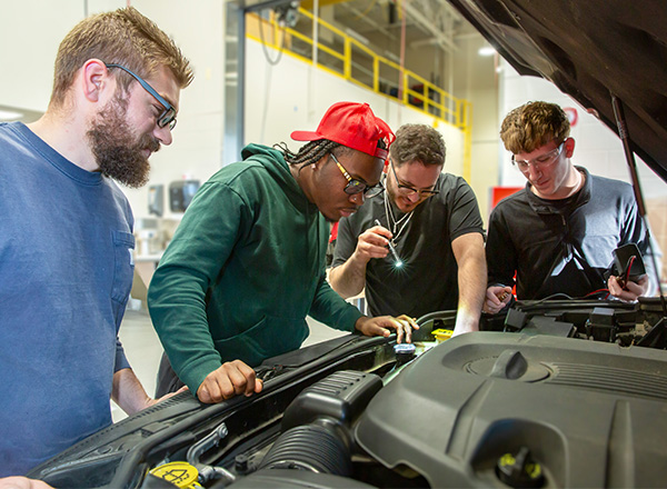 Students looking under the hood of a car.