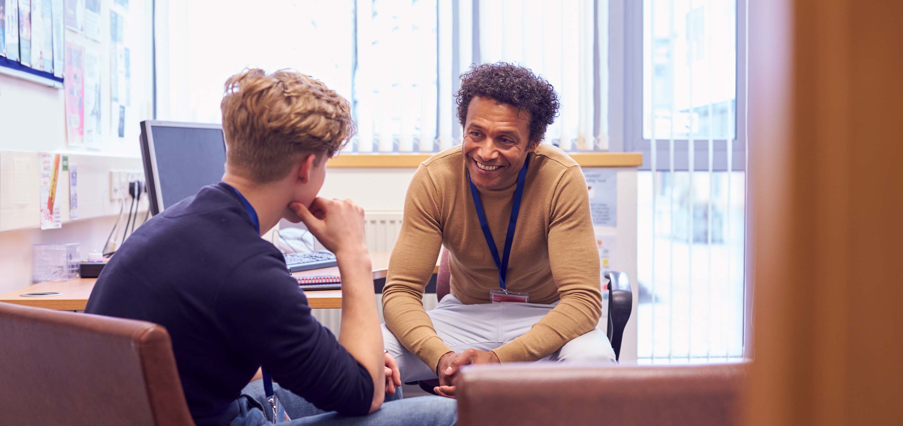 Smiling advisor speaking to student, both sitting in a well lit office