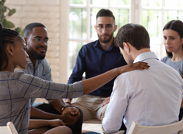 Rear view of a sad man being comforted by his support group.