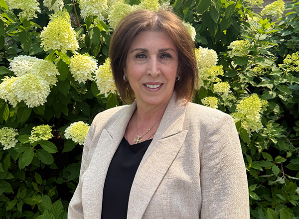 Kim Najarian portrait outdoors with a floral bush in the background.