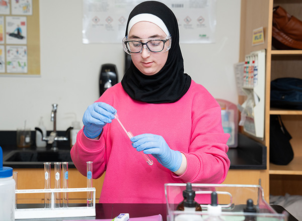 A chemistry student using a pipette to drip liquid into a test tube