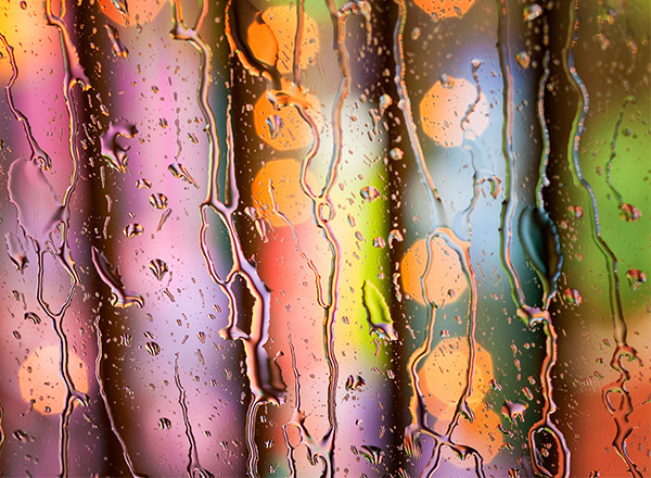 A photo of water dripping down a surface with a blurred rainbow color behind it.
