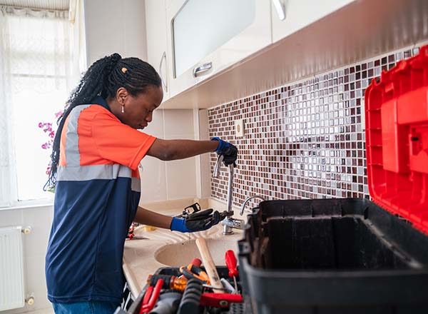 Plumber wearing gloves, fixing a leak in the kitchen sink of a house.