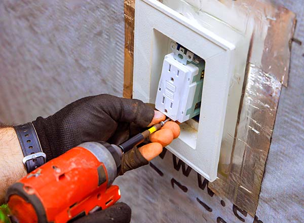 Close-up of electrician, wearing gloves, installing an outlet with a red drill.