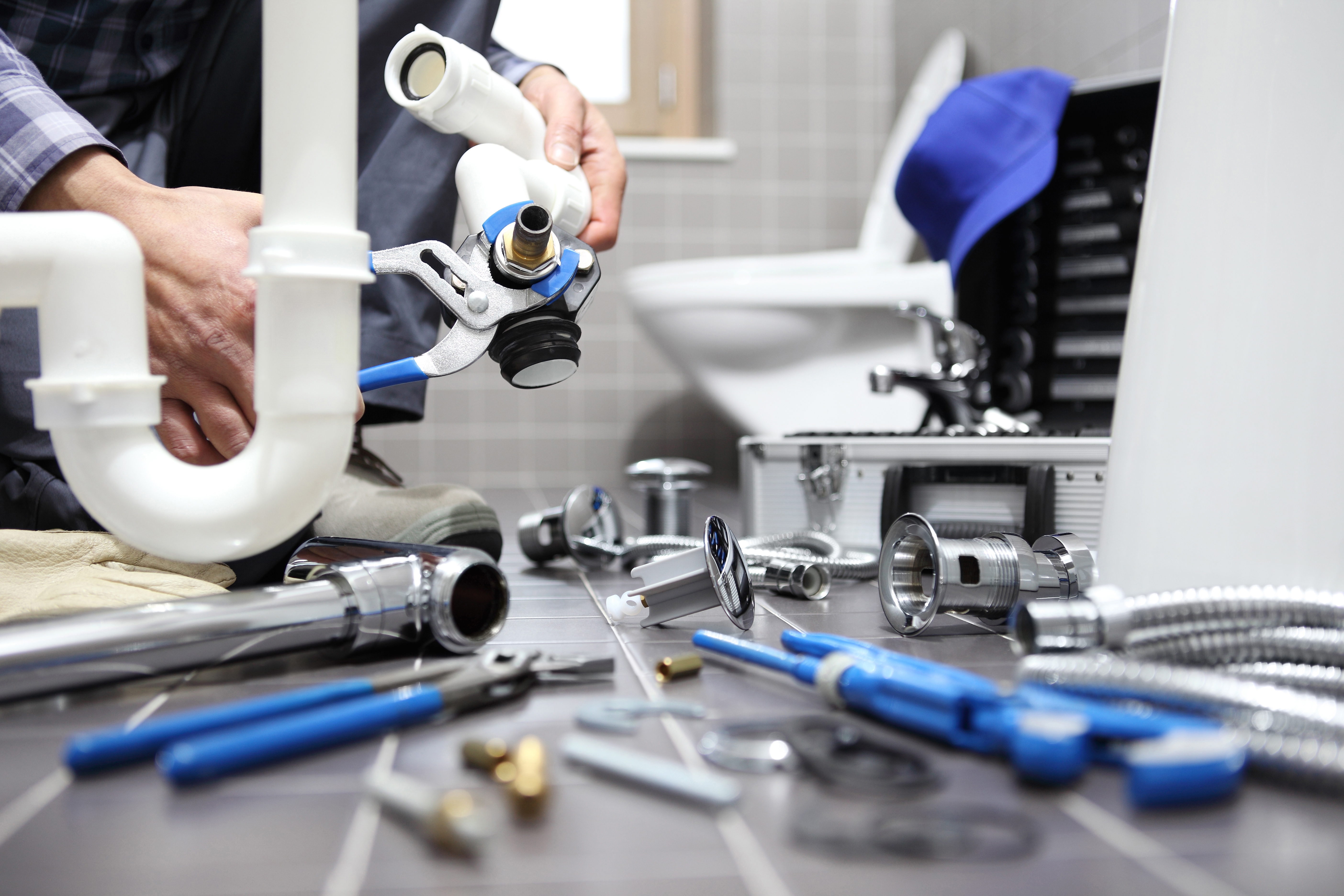 Plumber fixing bathroom plumbing, floor covered in different pipes, tools, and attachments.