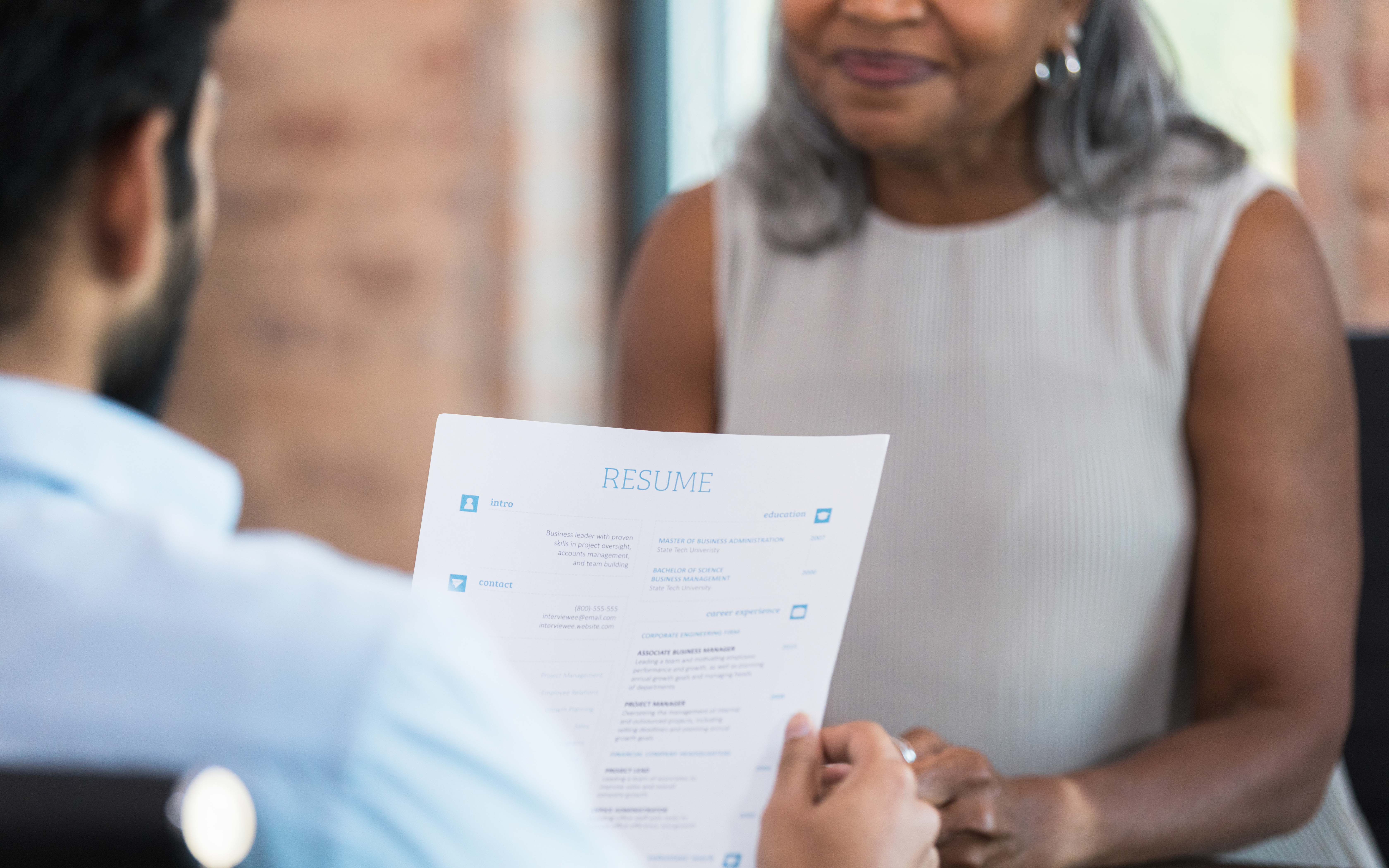 Two people sitting across from each other at a table, one holding a paper resume